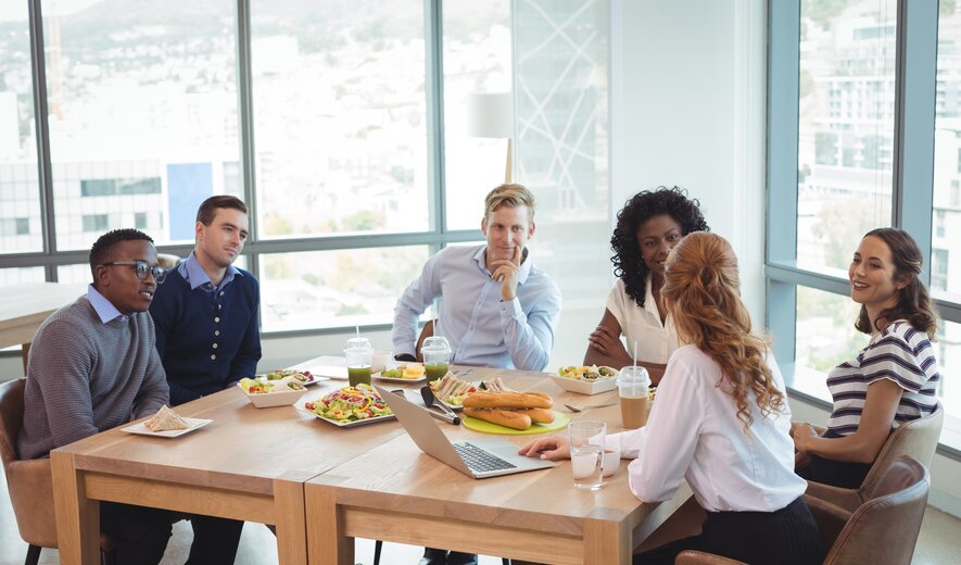 Eine Gruppe von Menschen sitzt gemeinsam an einem Tisch zu einem ungezwungenen Business-Lunch und bespricht etwas in entspannter Atmosphäre.