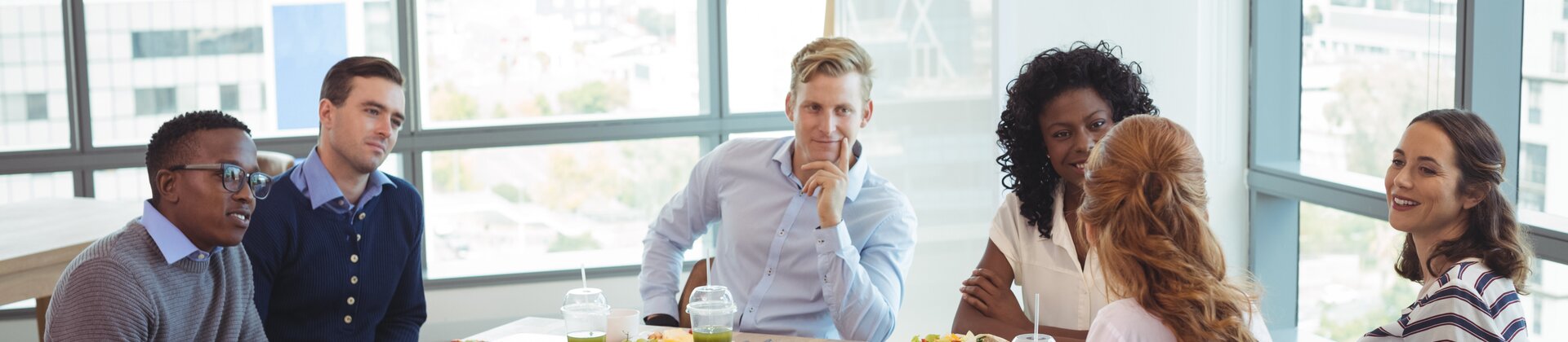 Eine Gruppe von Menschen sitzt gemeinsam an einem Tisch zu einem ungezwungenen Business-Lunch und bespricht etwas in entspannter Atmosphäre.