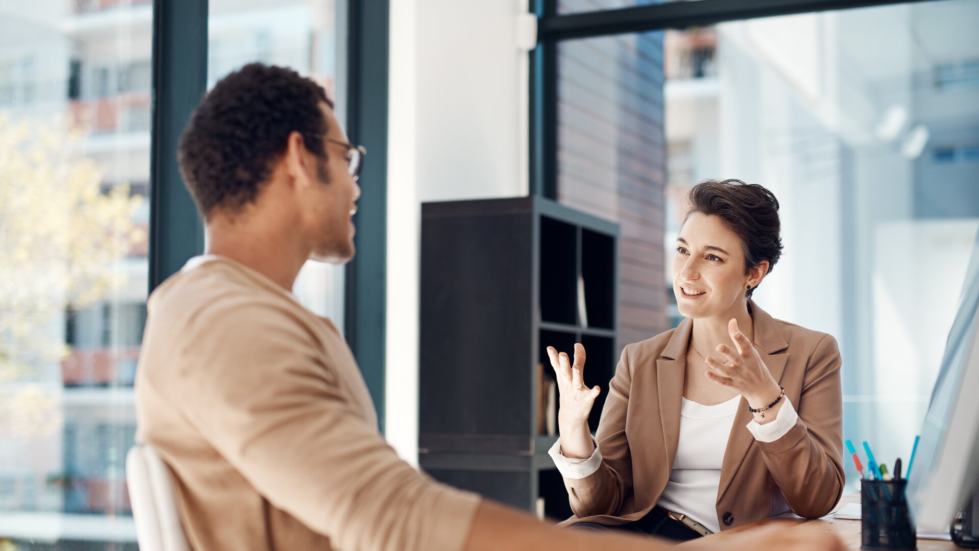 Eine Frau und ein Mann sitzen sich in einem modernen Büro gegenüber und führen ein engagiertes, gestenreiches Gespräch.