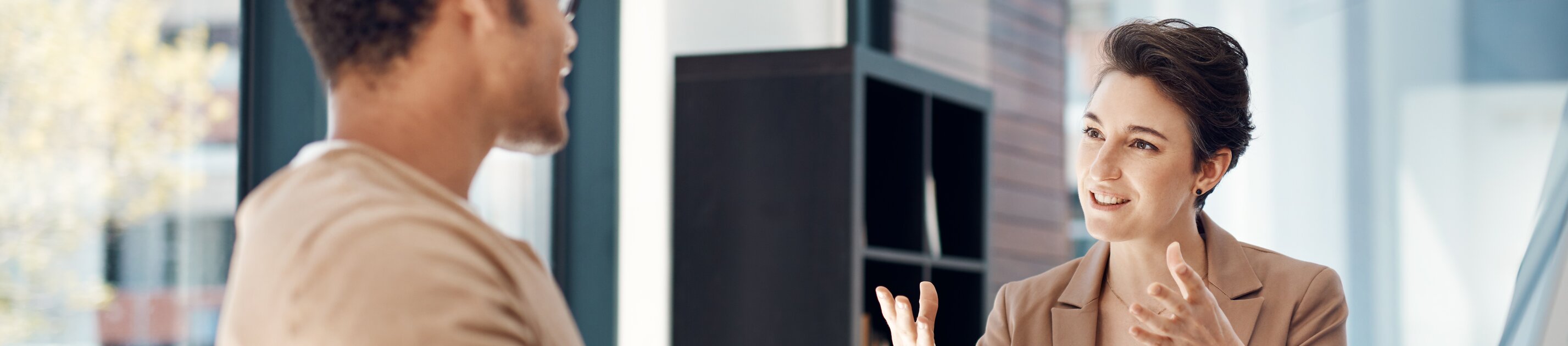 Eine Frau und ein Mann sitzen sich in einem modernen Büro gegenüber und führen ein engagiertes, gestenreiches Gespräch.