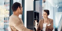 Eine Frau und ein Mann sitzen sich in einem modernen Büro gegenüber und führen ein engagiertes, gestenreiches Gespräch.
