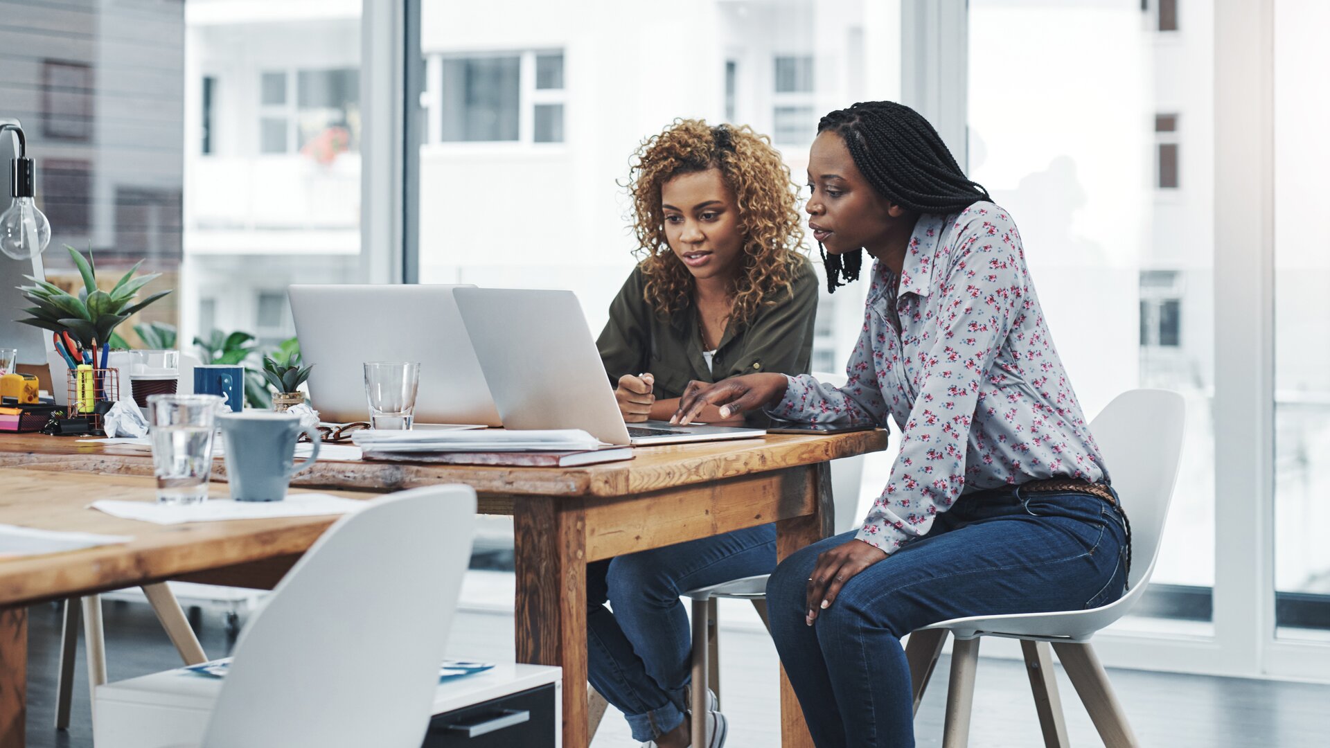 Zwei Personen arbeiten konzentriert gemeinsam an einem Laptop in einem modernen Büro.