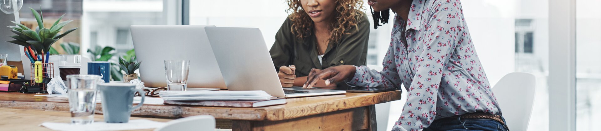 Zwei Personen arbeiten konzentriert gemeinsam an einem Laptop in einem modernen Büro.