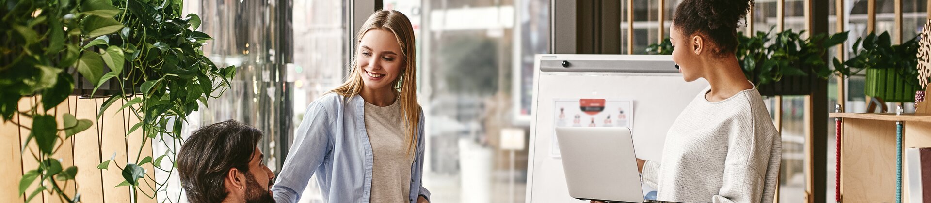 Drei Personen arbeiten in einer modernen, gemütlichen Umgebung zusammen, während eine Präsentation auf einem Flipchart gezeigt wird.