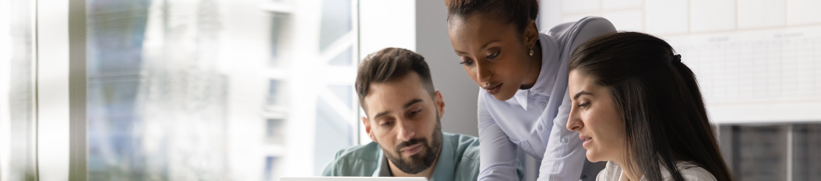 Drei Personen arbeiten gemeinsam konzentriert an einem Laptop und besprechen etwas im modernen Büro.