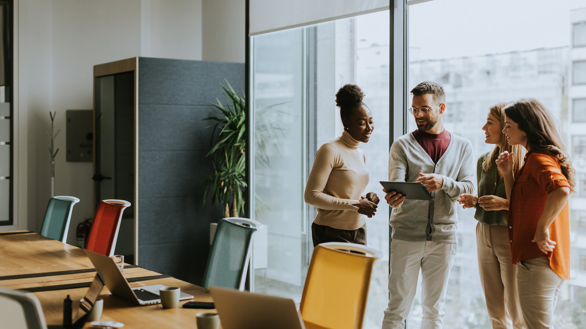 Eine kleine Gruppe steht entspannt zusammen und bespricht etwas anhand eines Tablets in einem modernen Besprechungsraum.
