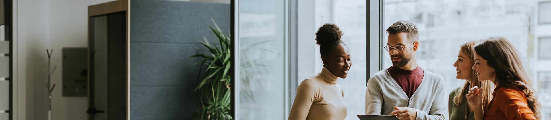 Eine kleine Gruppe steht entspannt zusammen und bespricht etwas anhand eines Tablets in einem modernen Besprechungsraum.