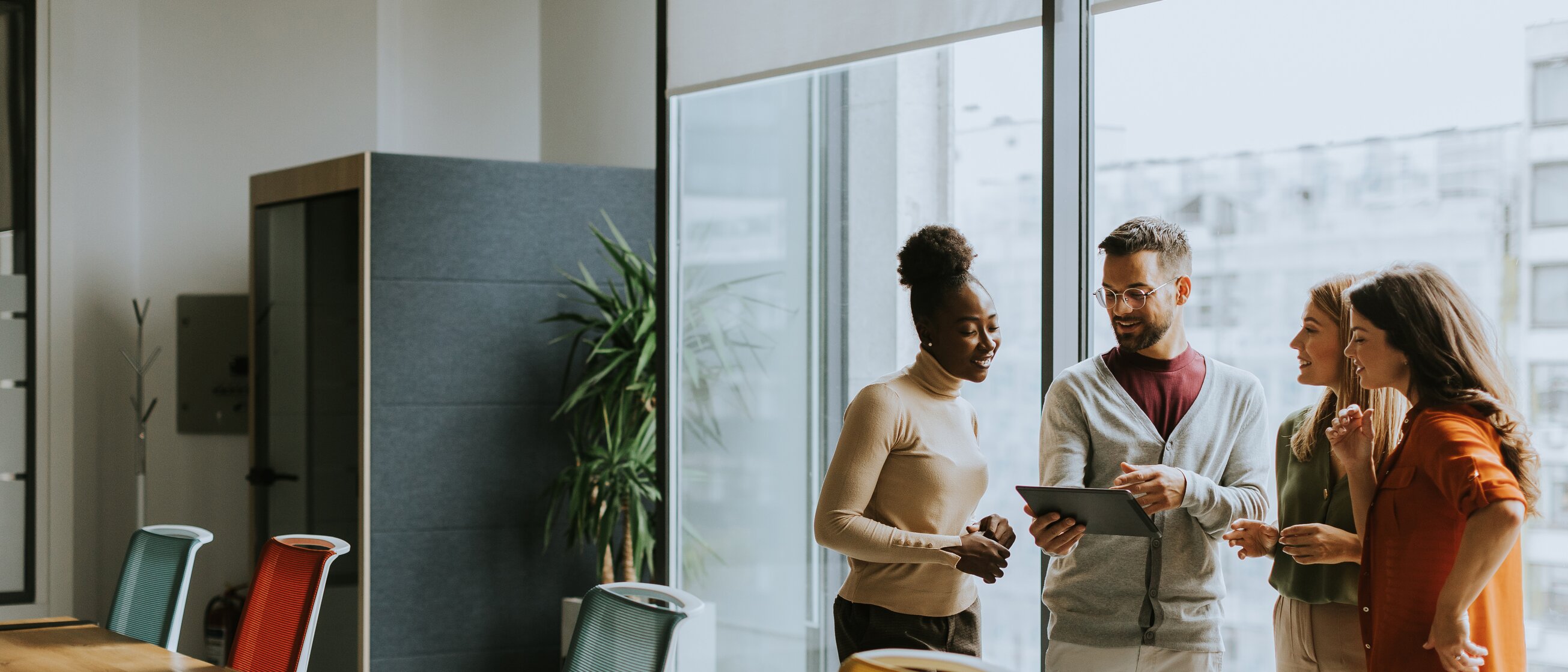 Vier Personen stehen im Büro und besprechen Inhalte an einem Tablet – Symbol für Weiterbildung und Coaching für Ausbilderinnen und Ausbilder.