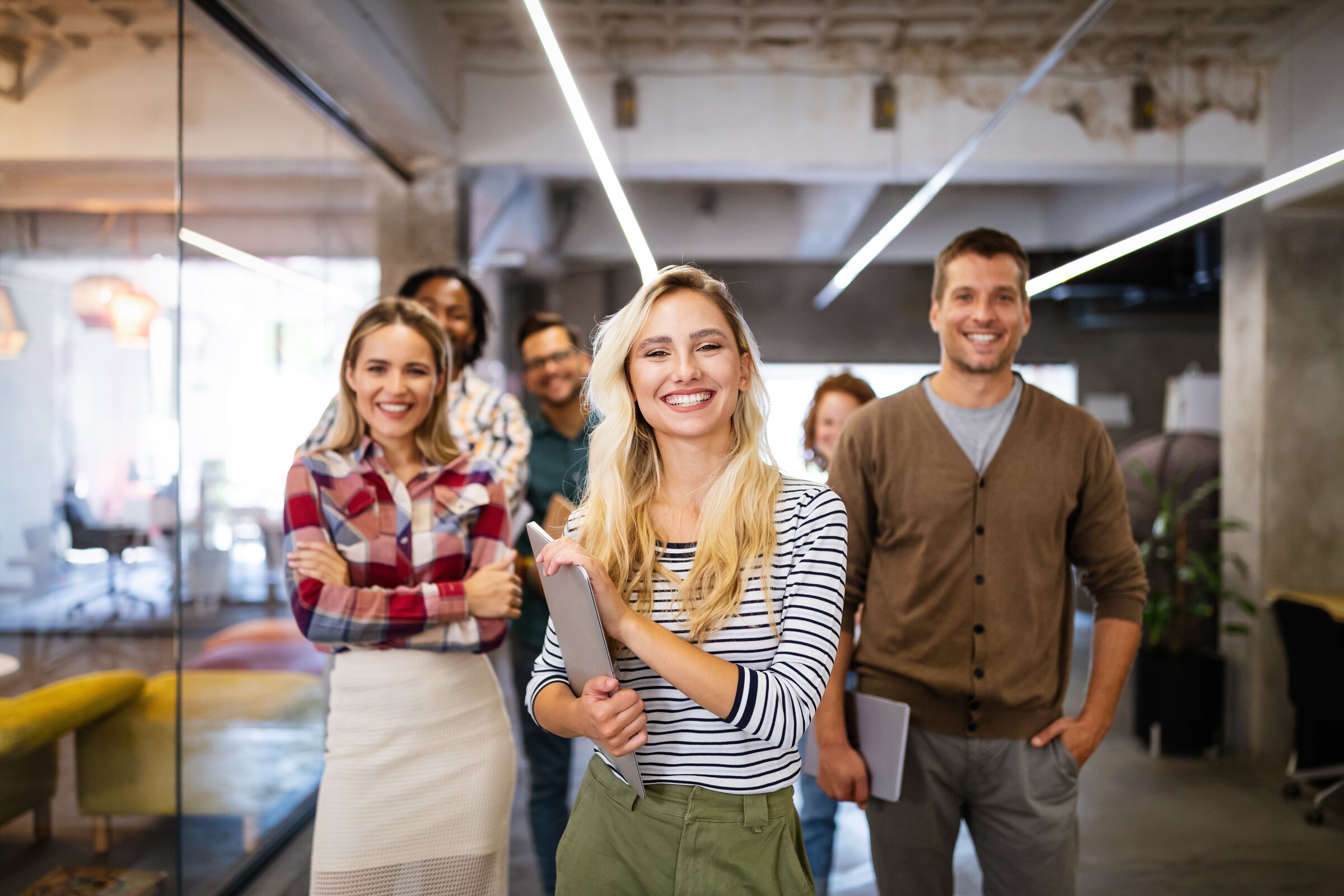Gruppe junger Menschen steht lächelnd im modernen Büro – Symbol für motivierte Ausbilderinnen und Ausbilder, die als Coach und Vorbild agieren.