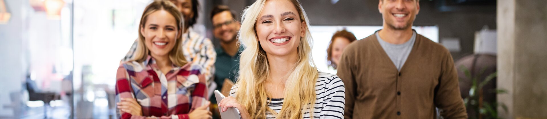 Eine fröhliche Gruppe junger Menschen steht gemeinsam in einem modernen Büro und wirkt motiviert und gut gelaunt.