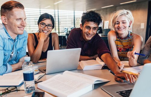 Weiterbildung für Azubis: Eine Gruppe junger Menschen sitzt an einem Tisch mit Laptops und Büchern vor sich. 