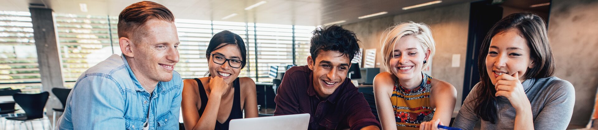 Weiterbildung für Auszubildende: Eine Gruppe Azubis sitzt in einer Lerngruppe vor einem Laptop. Ein junger Mann zeigt auf den Bildschirm von einem Laptop und erklärt den anderen Azubis etwas.