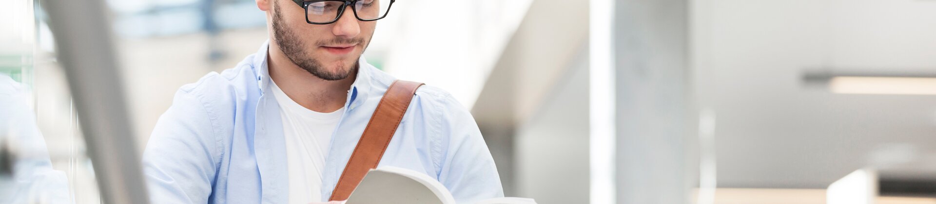 Ein junger Mann liest konzentriert in einem Buch in einer modernen Bibliothek.