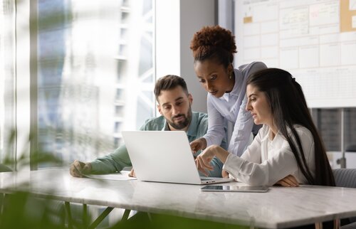 Drei Personen arbeiten gemeinsam konzentriert an einem Laptop und besprechen etwas im modernen Büro.