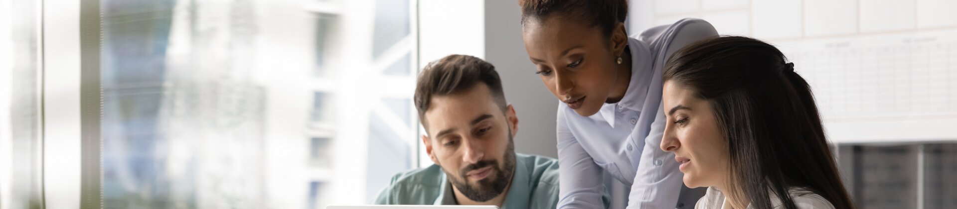 Drei Personen arbeiten gemeinsam konzentriert an einem Laptop und besprechen etwas im modernen Büro.