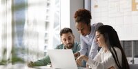 Drei Personen arbeiten gemeinsam konzentriert an einem Laptop und besprechen etwas im modernen Büro.