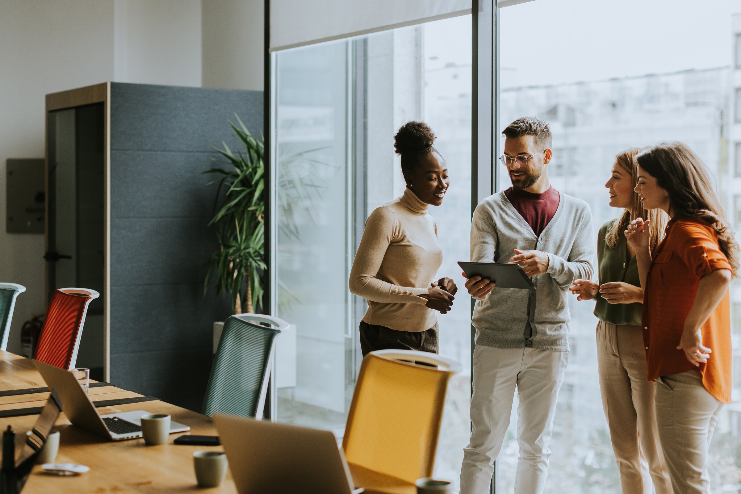 Eine kleine Gruppe steht entspannt zusammen und bespricht etwas anhand eines Tablets in einem modernen Besprechungsraum.