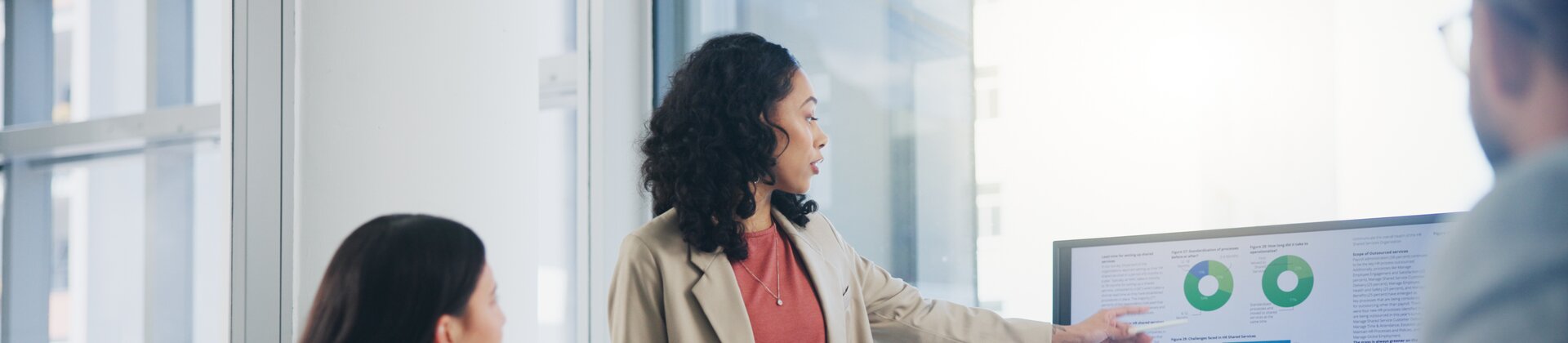 Eine Frau präsentiert ihrem Team Geschäftsgrafiken auf einem großen Bildschirm.