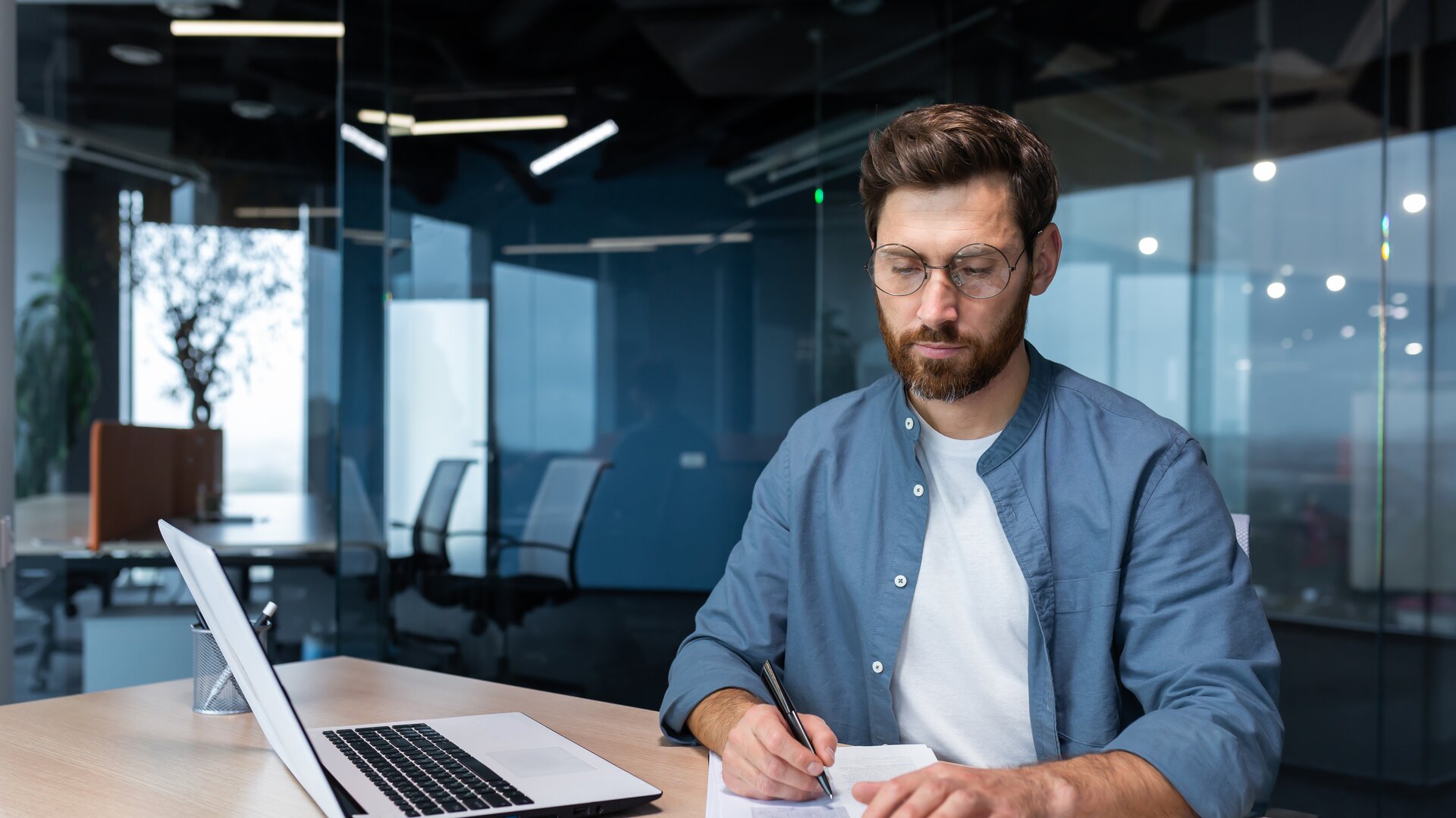 Ein Mann arbeitet konzentriert an seinem Schreibtisch, nutzt Laptop, Notizen und Taschenrechner für seine Aufgaben.
