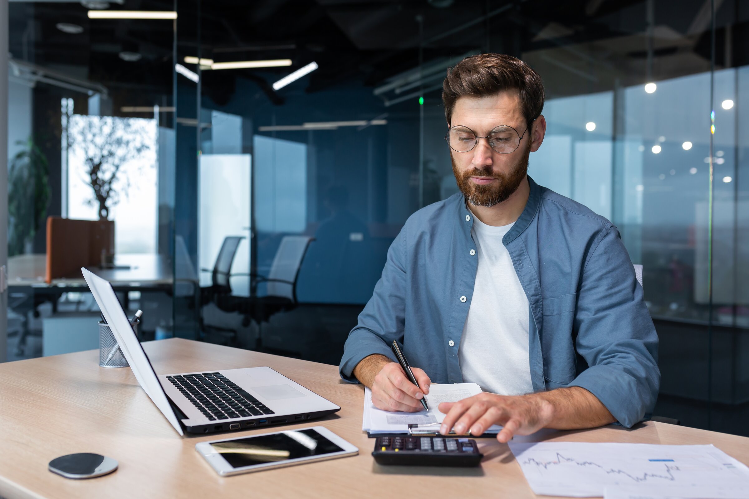 Mann arbeitet konzentriert mit Laptop und Unterlagen im Büro als Symbol für Bilanzbuchhaltung