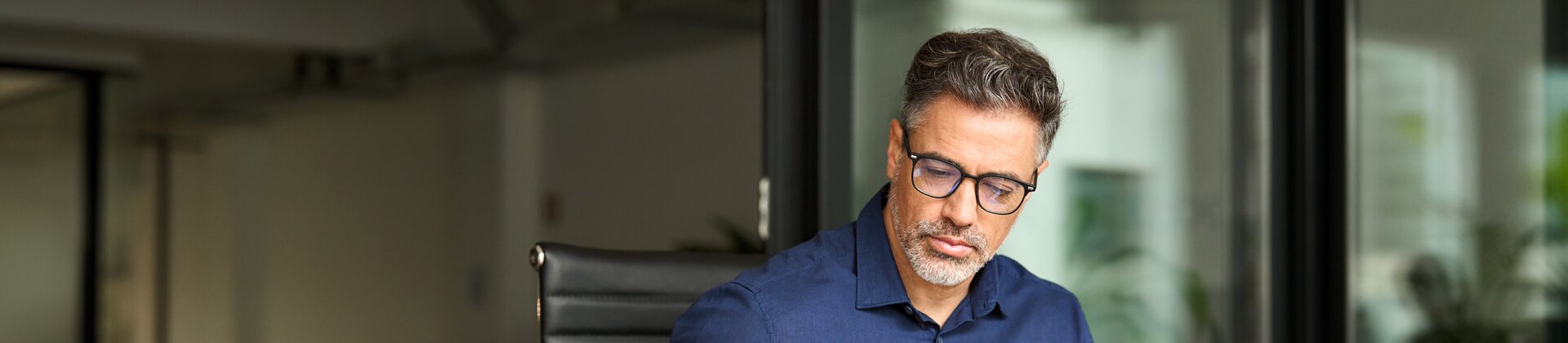 Ein Mann arbeitet konzentriert am Schreibtisch und prüft Unterlagen neben seinem Laptop.