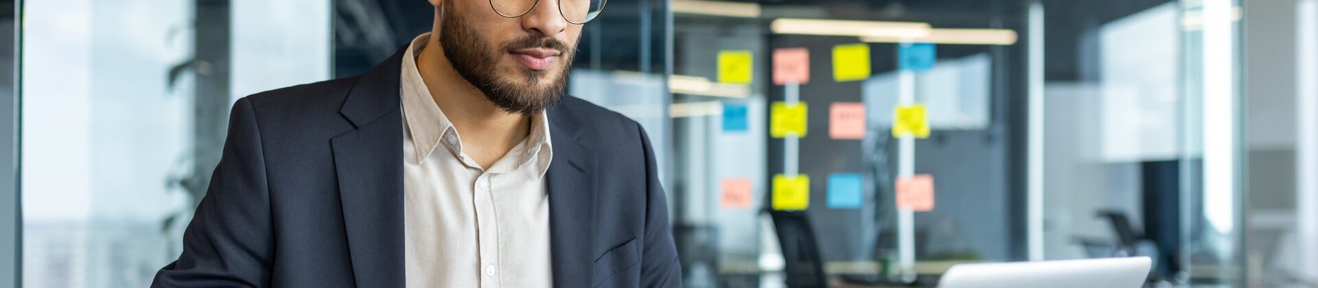 Ein Mann arbeitet konzentriert an seinem Laptop und macht sich dabei Notizen.