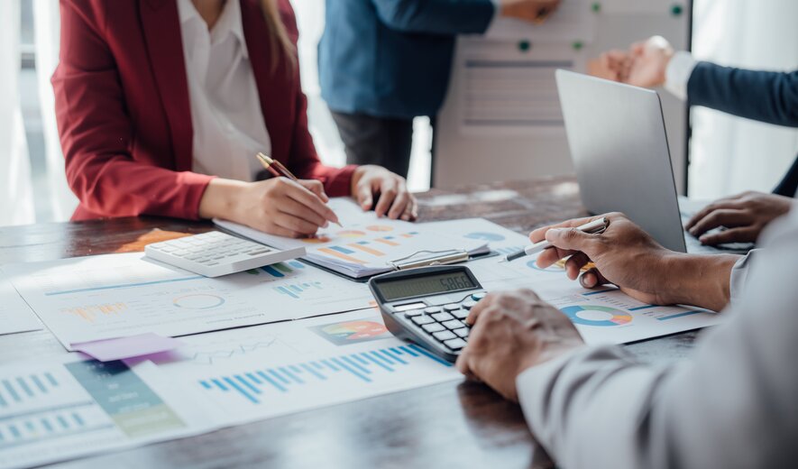 Das Bild zeigt mehrere Personen, die gemeinsam Finanz- und Diagrammdaten besprechen und auswerten.