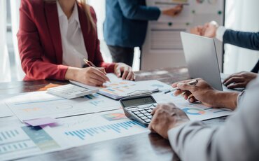 Geschäftsleute vergleichen Finanzdaten und Diagramme – Darstellung für IHK-Weiterbildungen in Finanzanlagen und Versicherungen zur sicheren Bewertung von Chancen und Risiken.