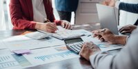 Das Bild zeigt mehrere Personen, die gemeinsam Finanz- und Diagrammdaten besprechen und auswerten.