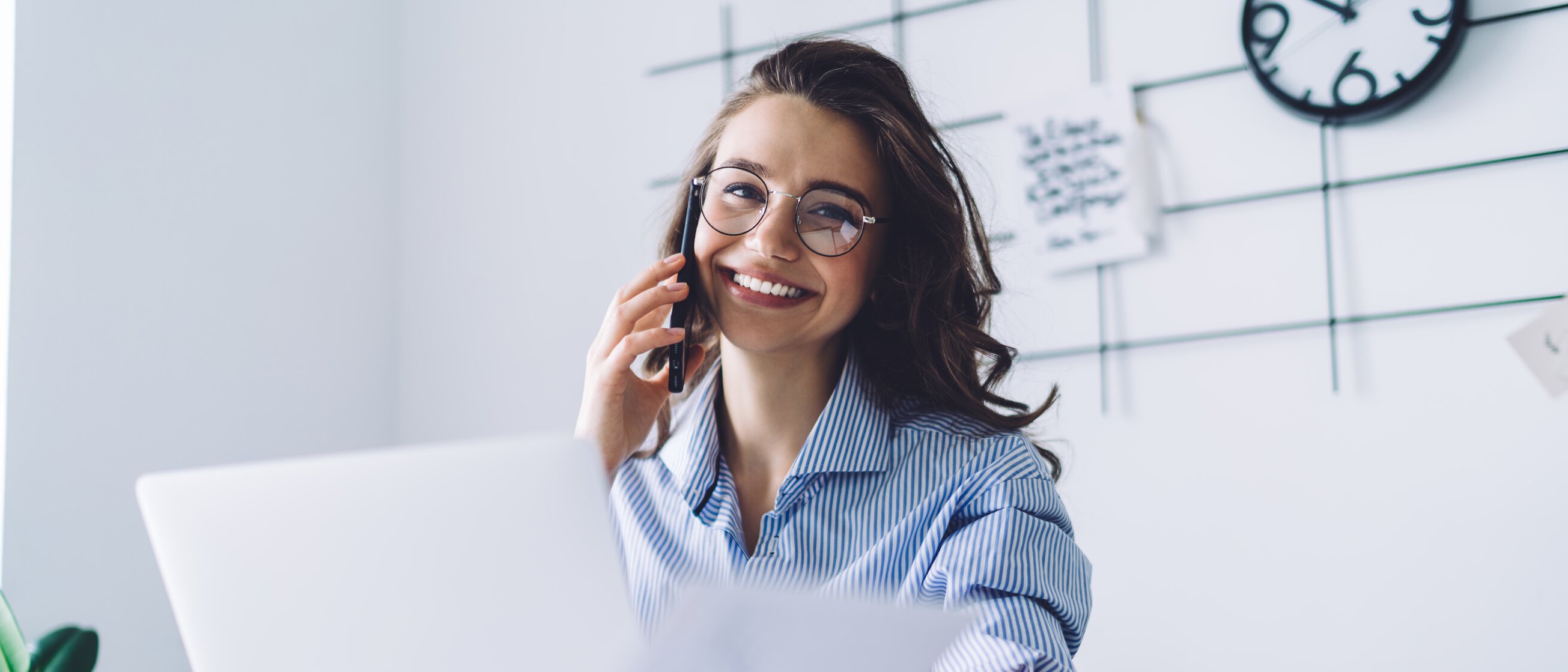Junge Frau arbeitet lächelnd im Büro, telefoniert und prüft Unterlagen am Laptop – Symbol für praxisnahe IHK-Weiterbildungen im Rechnungswesen und Finanzbuchhaltung für mehr Sicherheit im Umgang mit Unternehmenszahlen.