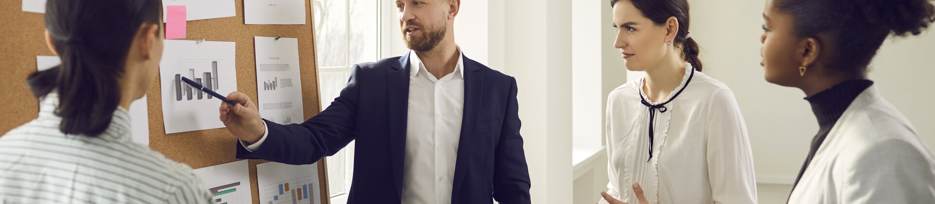 Ein Mann präsentiert seinem Team Diagramme an einer Pinnwand.