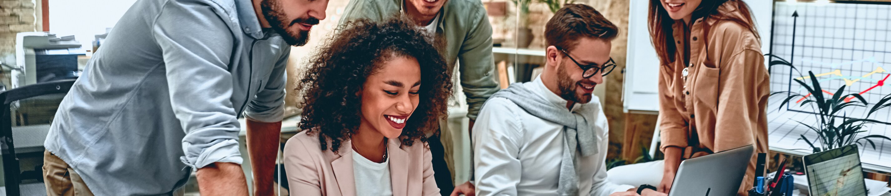 Eine Gruppe junger Menschen arbeitet gut gelaunt gemeinsam an einem Projekt im Büro.