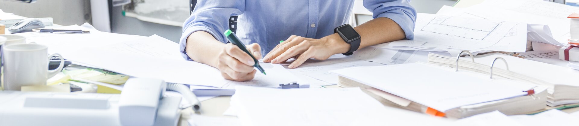 Eine Frau arbeitet fröhlich an einem Schreibtisch voller Unterlagen.