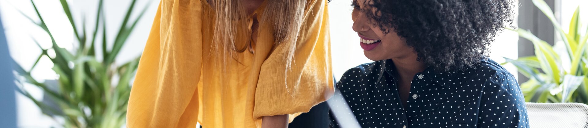 Zwei Frauen arbeiten gemeinsam an einem Laptop und besprechen etwas am Schreibtisch.