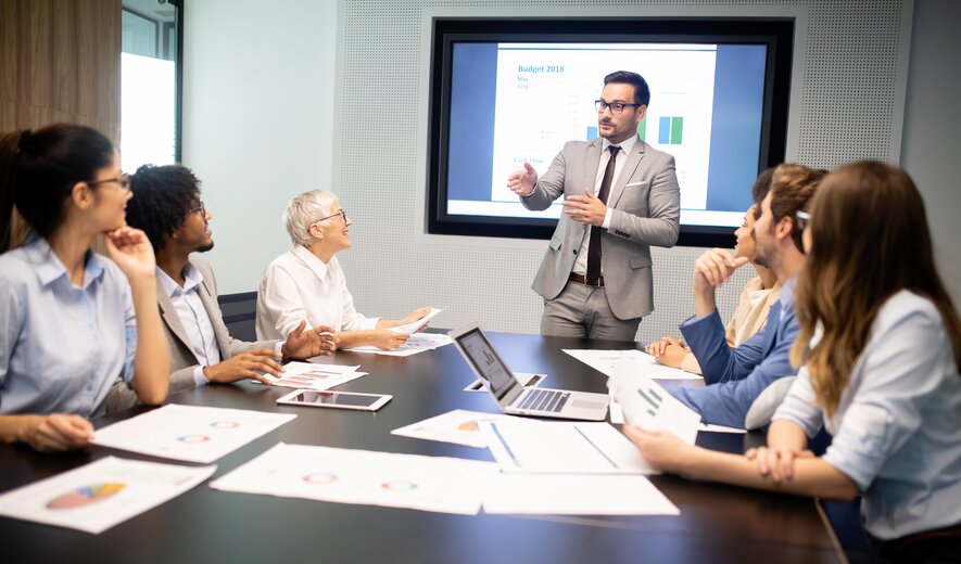 Eine Gruppe von Mitarbeitenden sitzt im Konferenzraum und hört einer Präsentation zu.