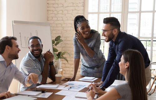 Ein Team von fünf Personen sitzt gemeinsam am Tisch und führt ein fröhliches, produktives Meeting.