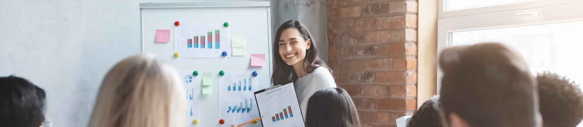 Eine Frau präsentiert ihrem Team gut sichtbar Diagramme und Ergebnisse an einem Whiteboard.
