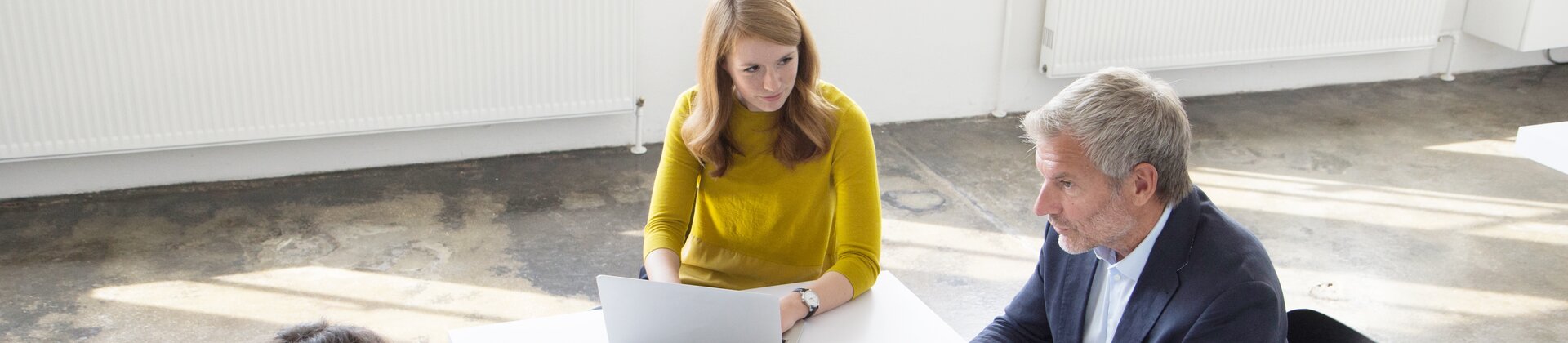 Das Bild zeigt drei Personen in einem hellen Besprechungsraum, die gemeinsam an digitalen Unterlagen arbeiten.