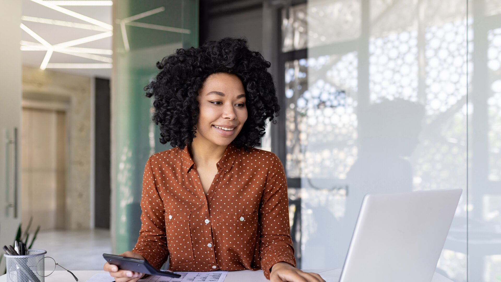 Das Bild zeigt eine Person, die konzentriert am Schreibtisch arbeitet und dabei sowohl einen Laptop als auch einen Taschenrechner benutzt.