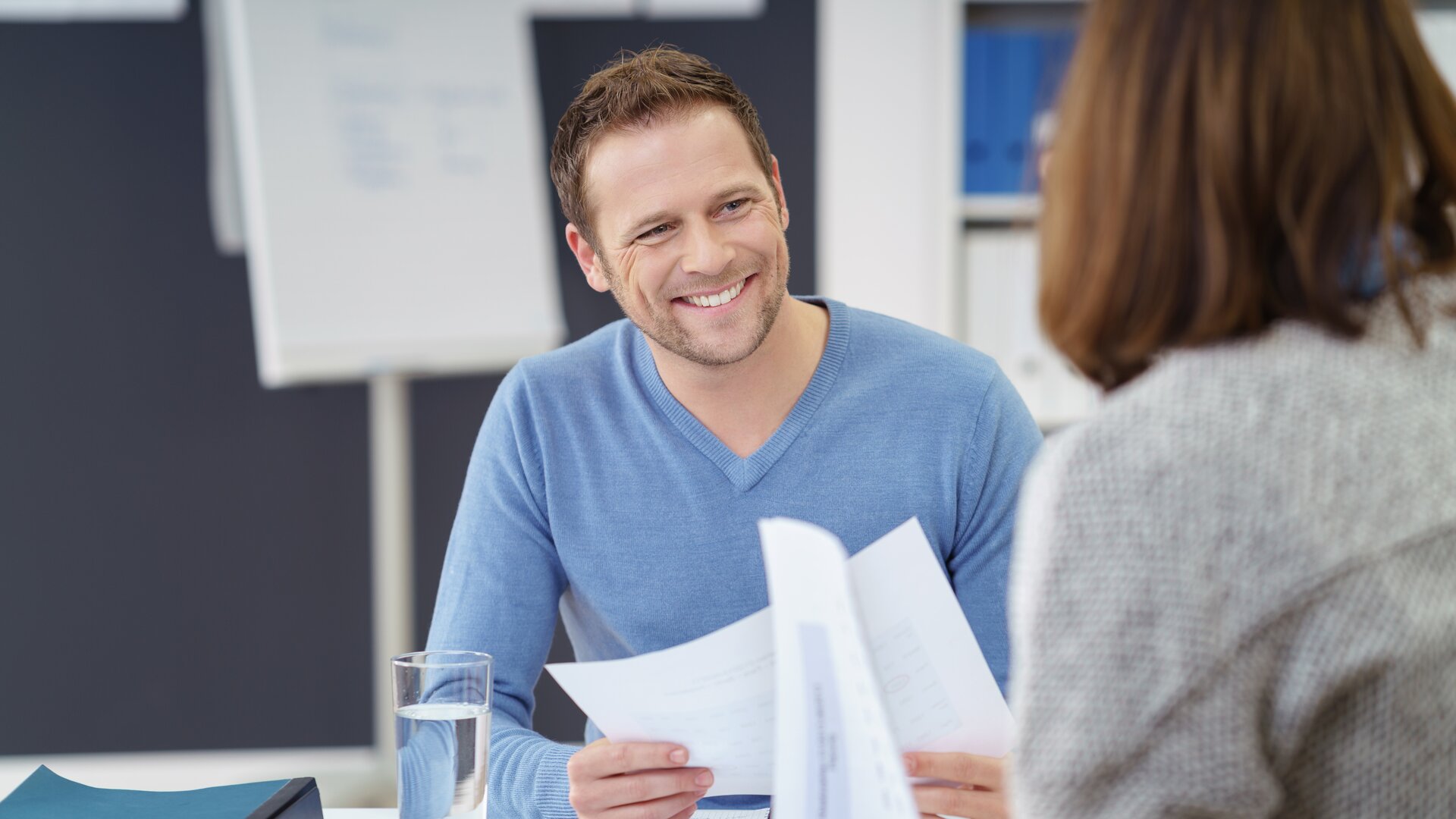 Ein Mann führt ein freundliches Gespräch, während er gemeinsam mit einer anderen Person Dokumente durchgeht.