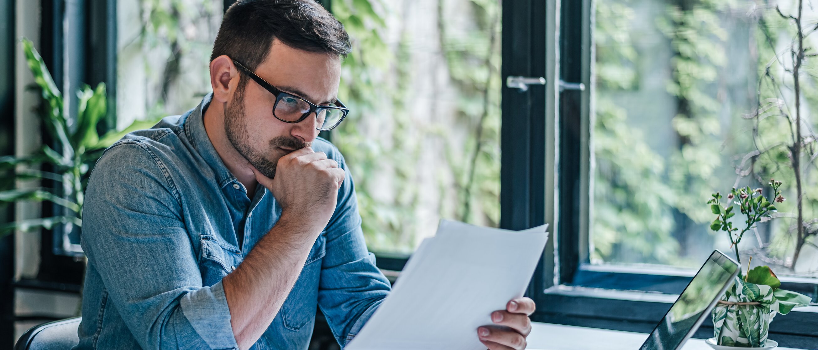 Ein Mann sitzt nachdenklich am Schreibtisch, prüft konzentriert Dokumente und arbeitet mit Laptop und Unterlagen – Symbol für die verantwortungsvolle Analyse und Umsetzung von Datenschutzrichtlinien.