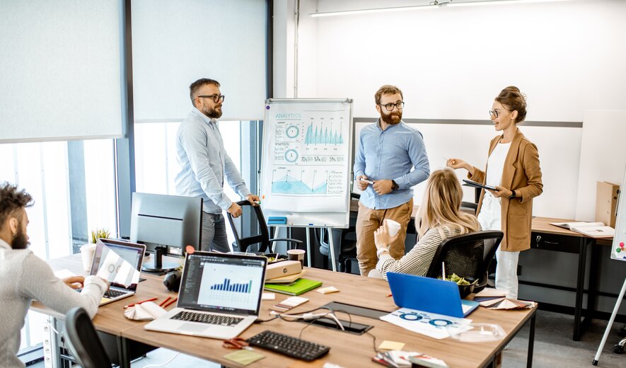 Eine kleine Gruppe arbeitet im modernen Büro gemeinsam an einer Präsentation und bespricht Analyseergebnisse.