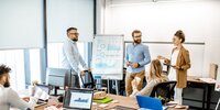 Eine kleine Gruppe arbeitet im modernen Büro gemeinsam an einer Präsentation und bespricht Analyseergebnisse.
