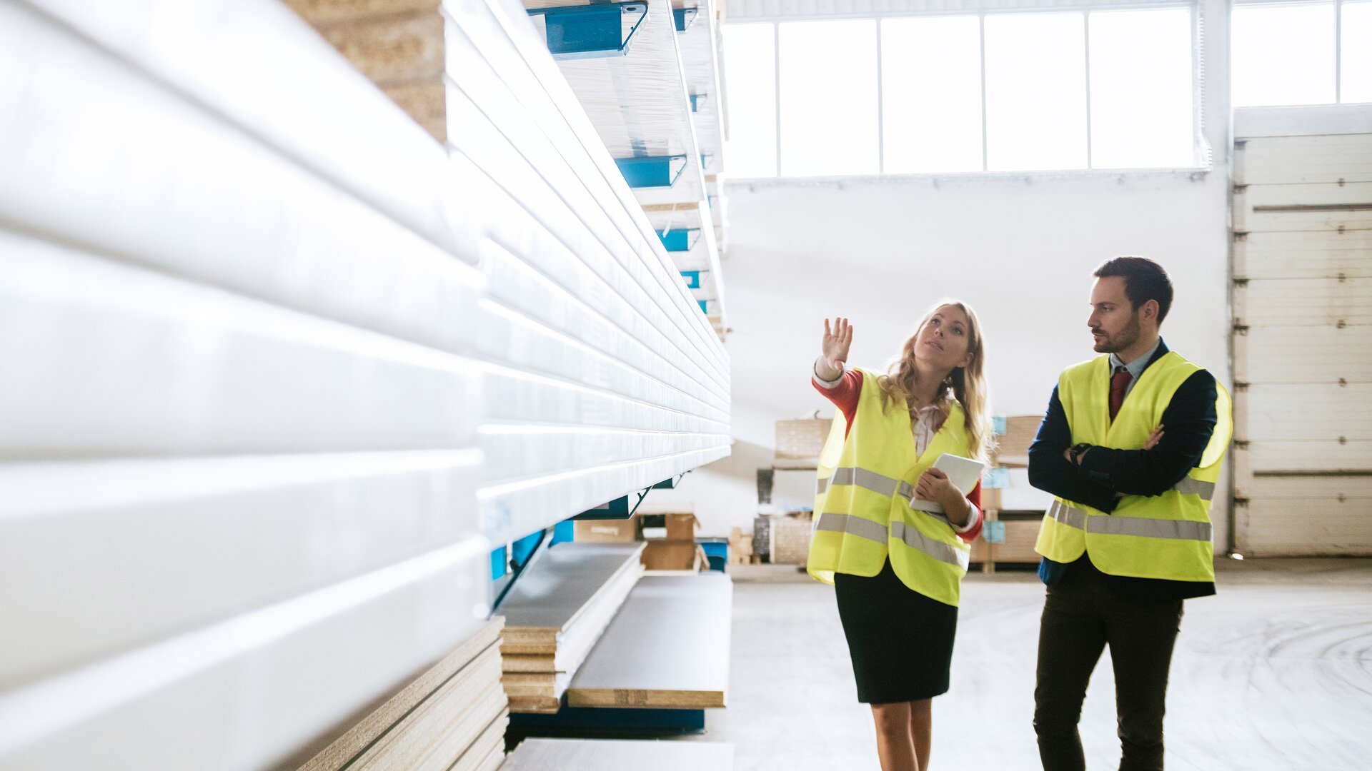 Eine Mitarbeiterin zeigt einem Kollegen in einer Lagerhalle verschiedene Materialien oder Bestände.