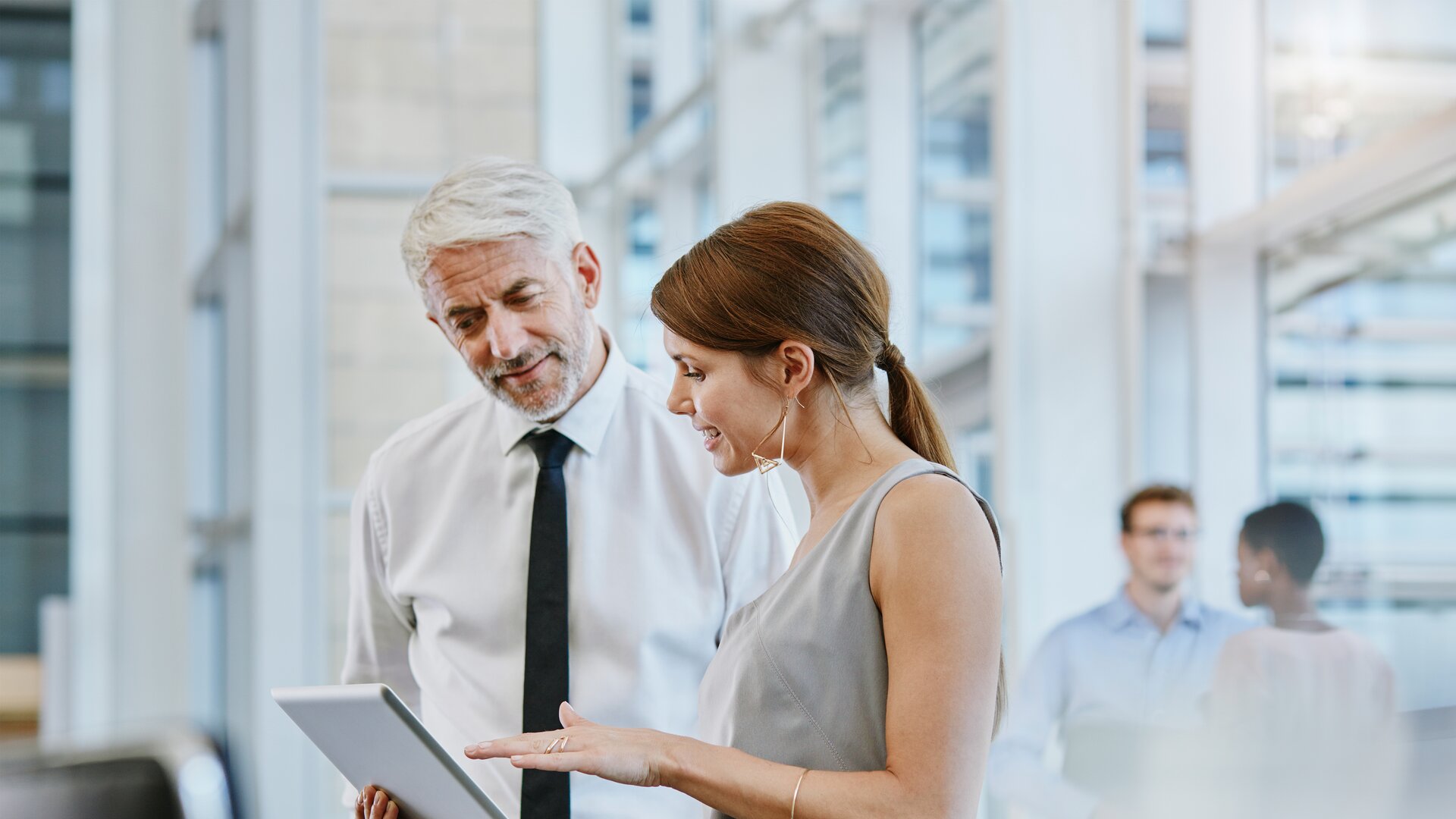 Eine Mitarbeiterin bespricht etwas auf einem Tablet mit einem Kollegen im Büro.