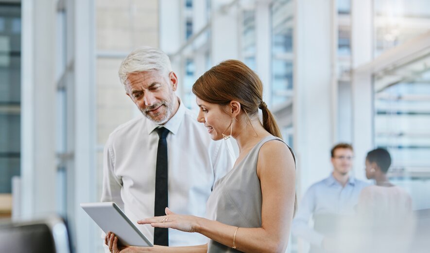 Eine Mitarbeiterin bespricht etwas auf einem Tablet mit einem Kollegen im Büro.