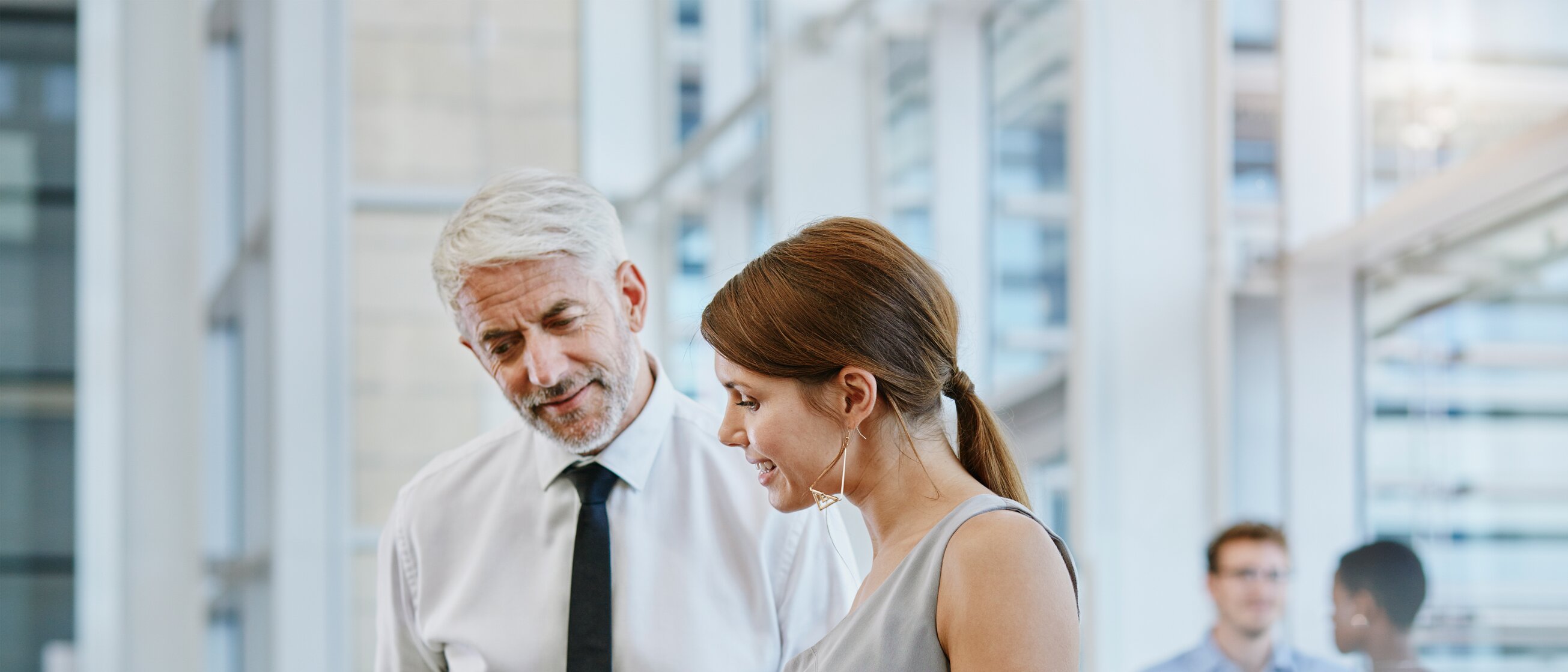 Zwei Berufstätige im Gespräch im modernen Büro, die gemeinsam Informationen auf einem Tablet besprechen – Symbol für erfolgreiche Kommunikation und strategisches Arbeiten im Einkauf.