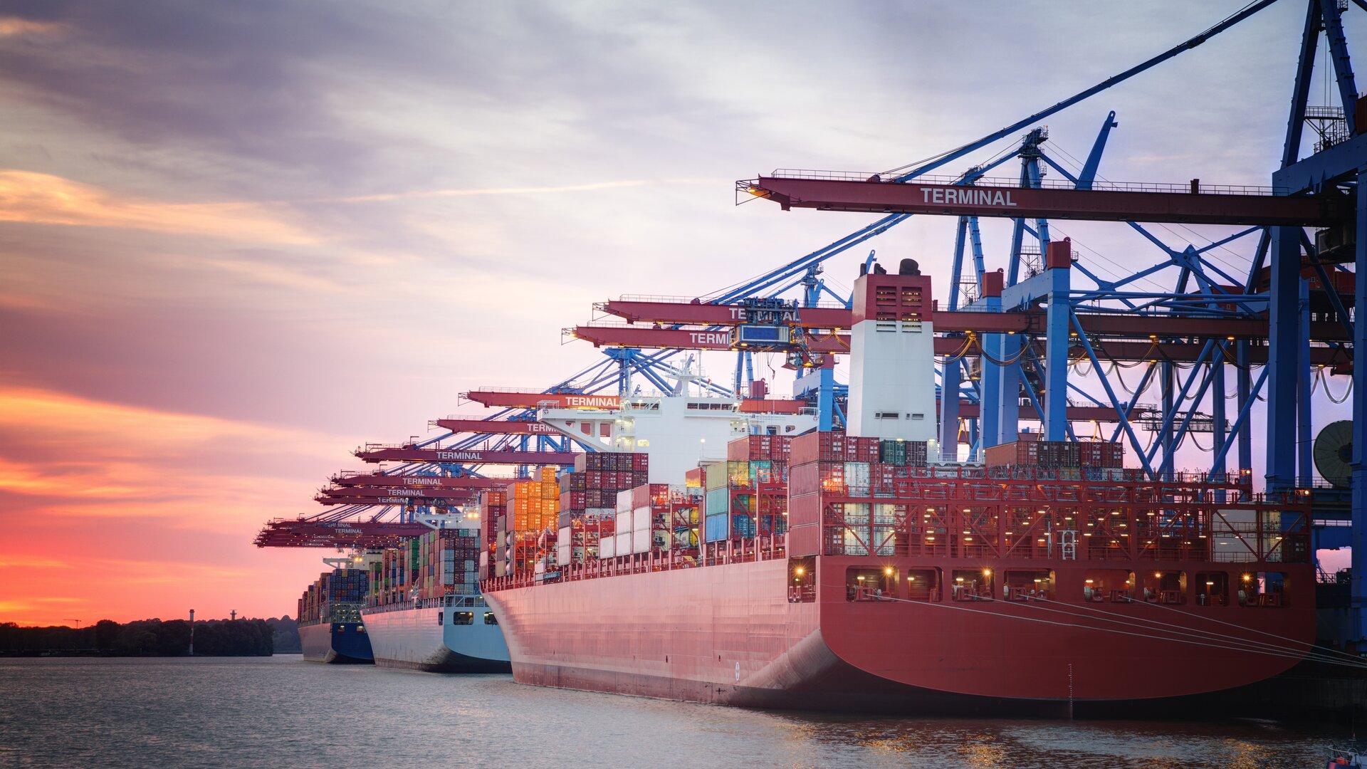 Ein großes Containerschiff wird bei Sonnenuntergang im Hafen von Kränen be- oder entladen.