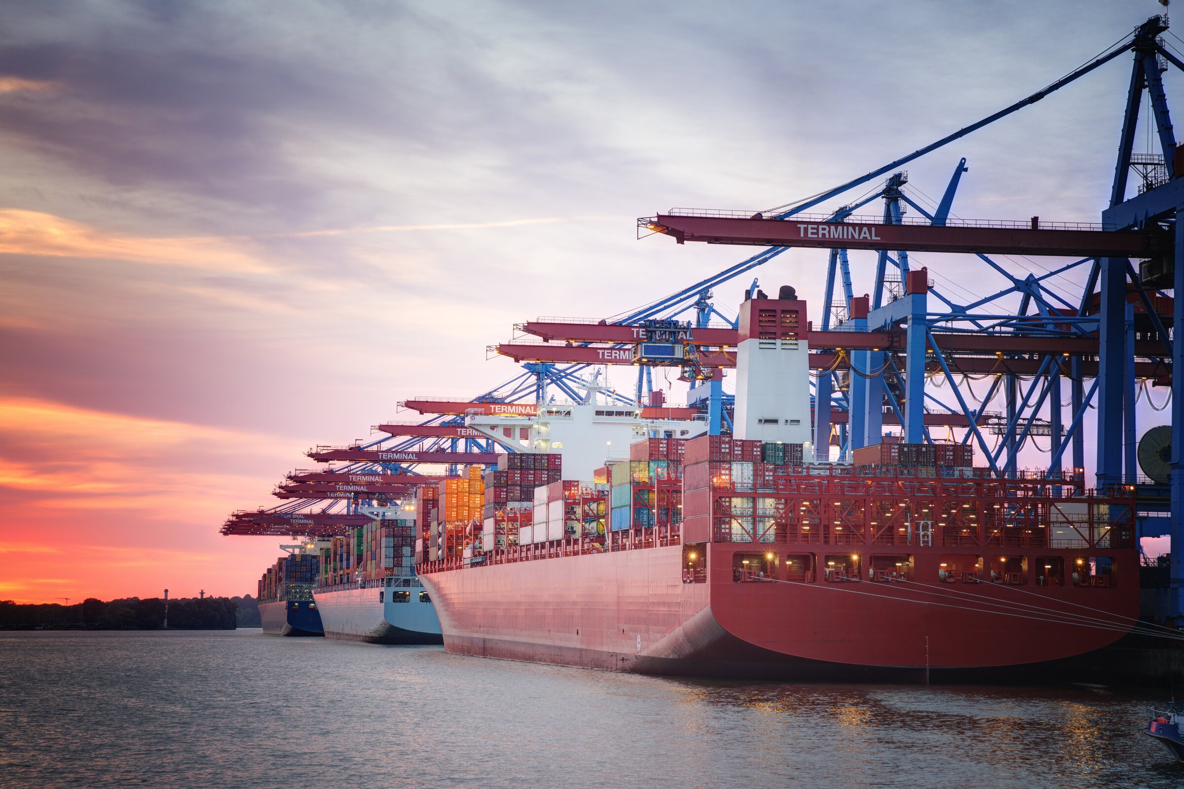Ein großes Containerschiff wird bei Sonnenuntergang im Hafen von Kränen be- oder entladen.
