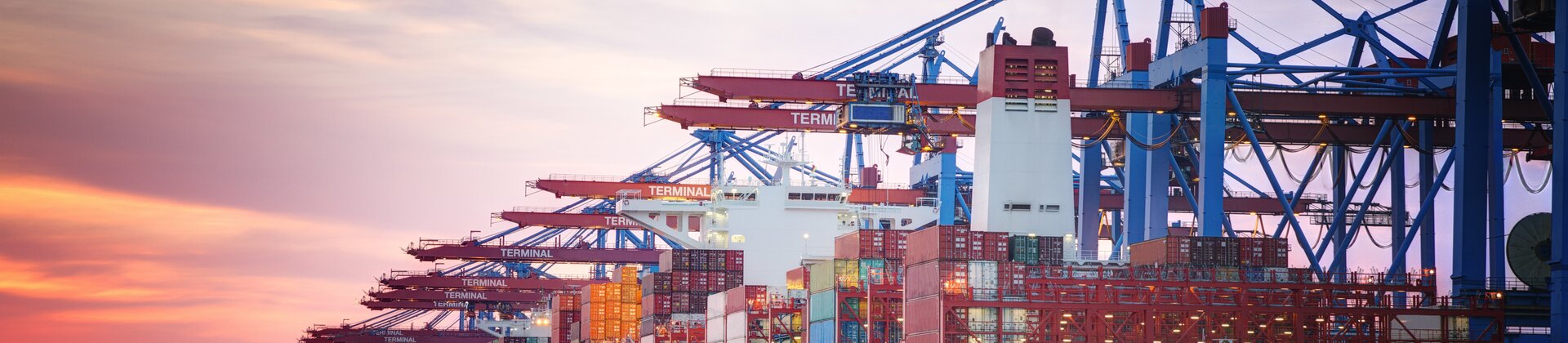 Ein großes Containerschiff wird bei Sonnenuntergang im Hafen von Kränen be- oder entladen.